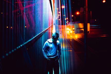 Jeune homme en sweat capuche de nuit dans une rue éclairée de néons de couleurs