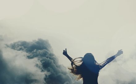 Femme levant les bras au ciel sur fond de nuages